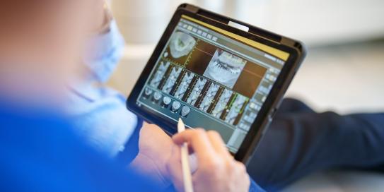 Zahnarzt betrachtet Röntgenbilder auf Tablet während Behandlung