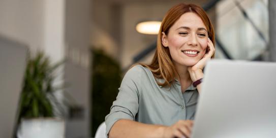 Frau arbeitet lächelnd am Laptop in modernem Büro.