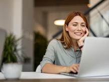 Frau arbeitet lächelnd am Laptop in modernem Büro.