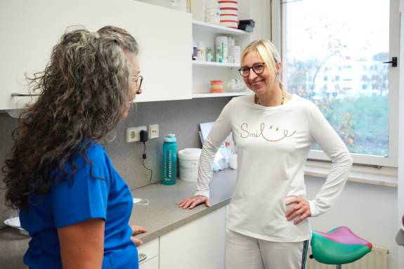 Zahnärztin spricht freundlich mit Patientin im Behandlungsraum.