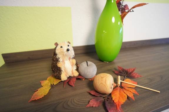 Herbstliche Dekoration mit Igel, Blättern und grüner Vase auf Tisch.