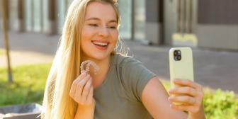 Frau macht Selfie und zeigt transparenten Zahnschienen-Aligner im Freien.