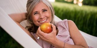 Frau entspannt in Hängematte und lächelt mit Apfel in der Hand.