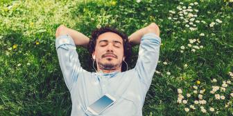 Mann liegt entspannt auf Wiese mit geschlossenen Augen und Kopfhörern.