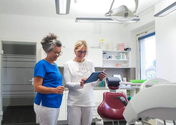 Zwei Zahnärztinnen betrachten gemeinsam Tablet im Behandlungsraum.