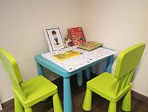 Kinder-Ecke mit Tisch, Stühlen und Büchern im Wartebereich.