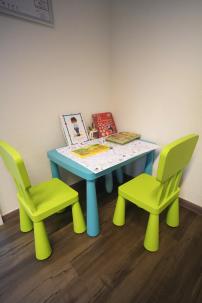 Kinder-Ecke mit Tisch, Stühlen und Büchern im Wartebereich.