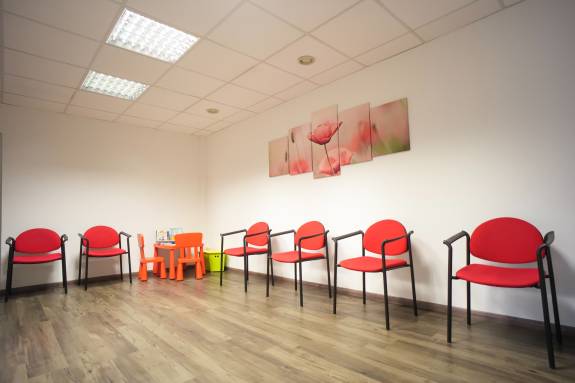 Wartezimmer mit roten Stühlen und Blumenbild an der Wand.